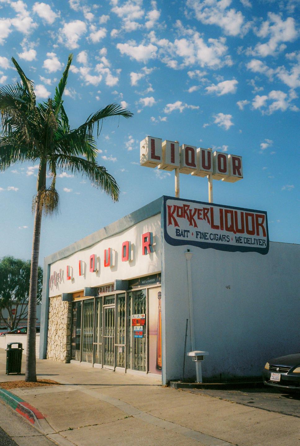 A liquor store with a palm tree in front of it stands under a blue sky with white clouds.
