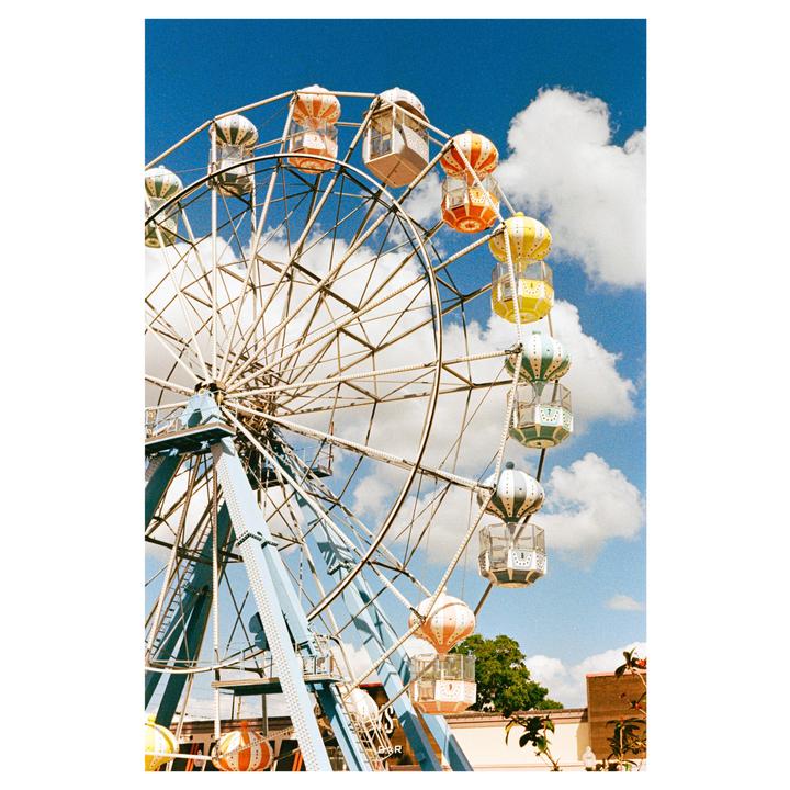 A colorful ferris wheel stands against a bright blue sky with white clouds.