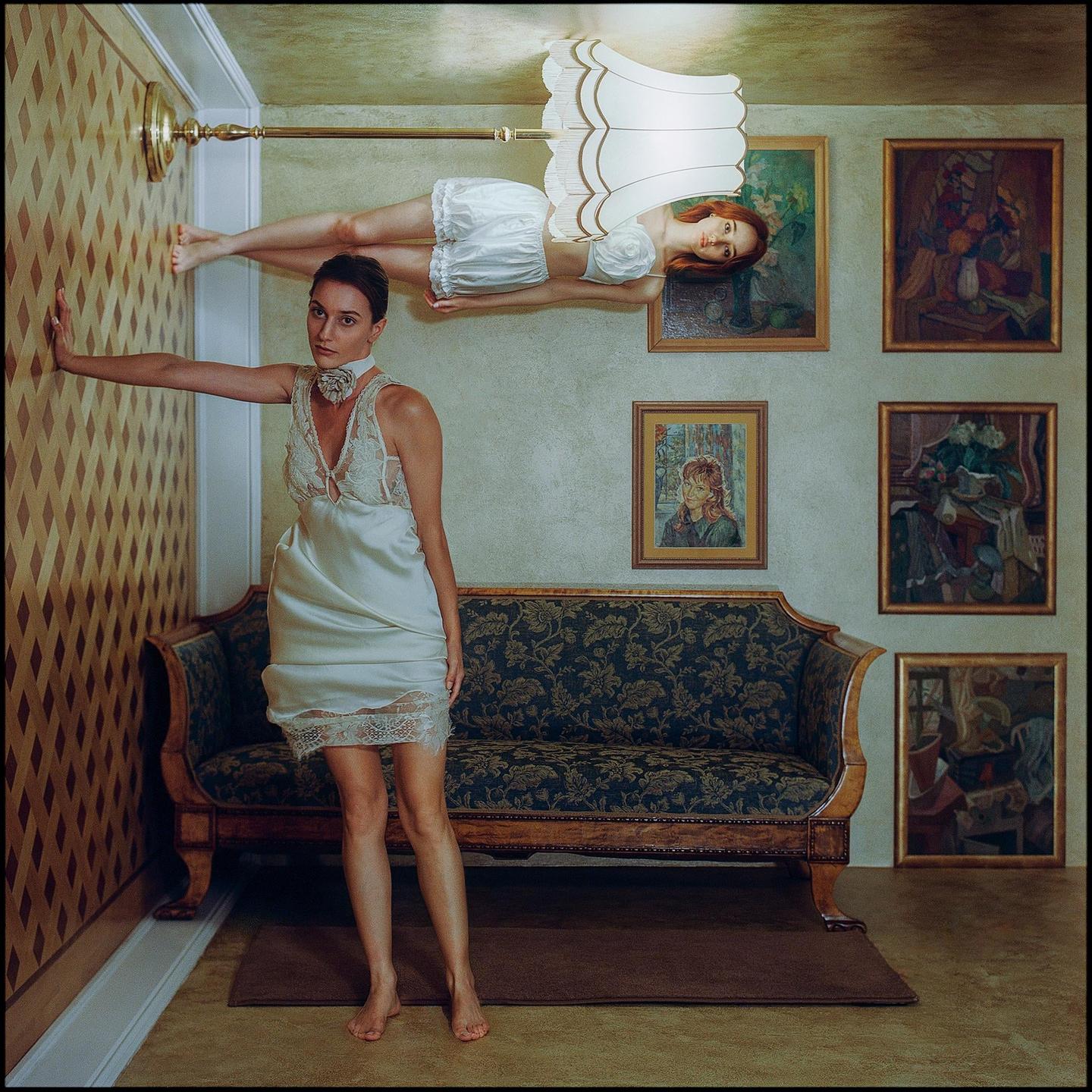 A woman stands on the floor while another woman floats upside down near the ceiling, holding onto a lamp.
