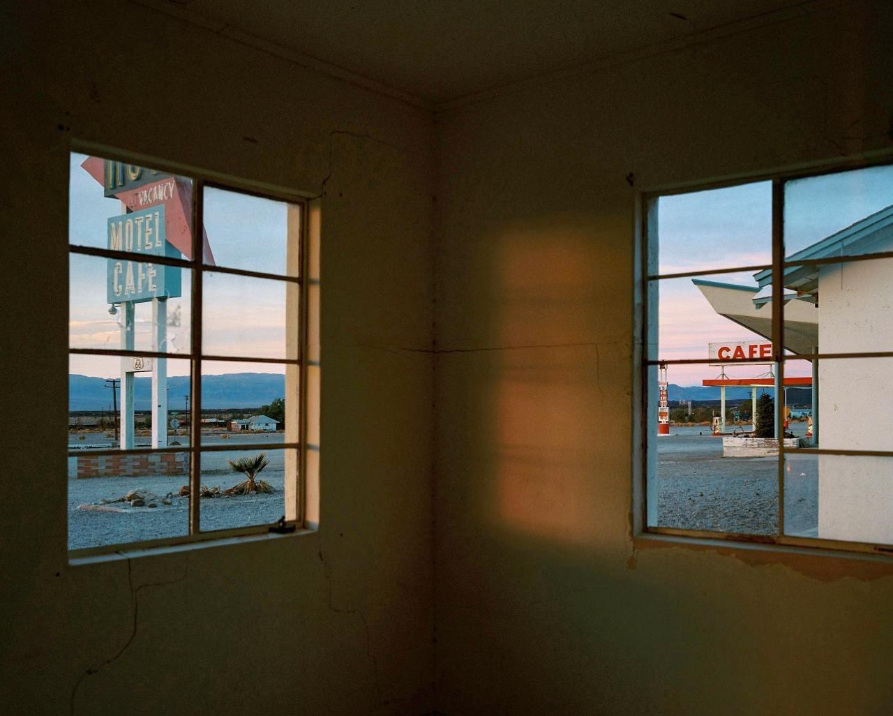 A motel and cafe are visible through two windows from inside a building at dusk.