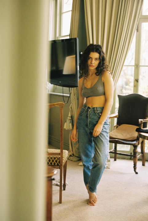 A woman stands barefoot in a room with a television and chairs.