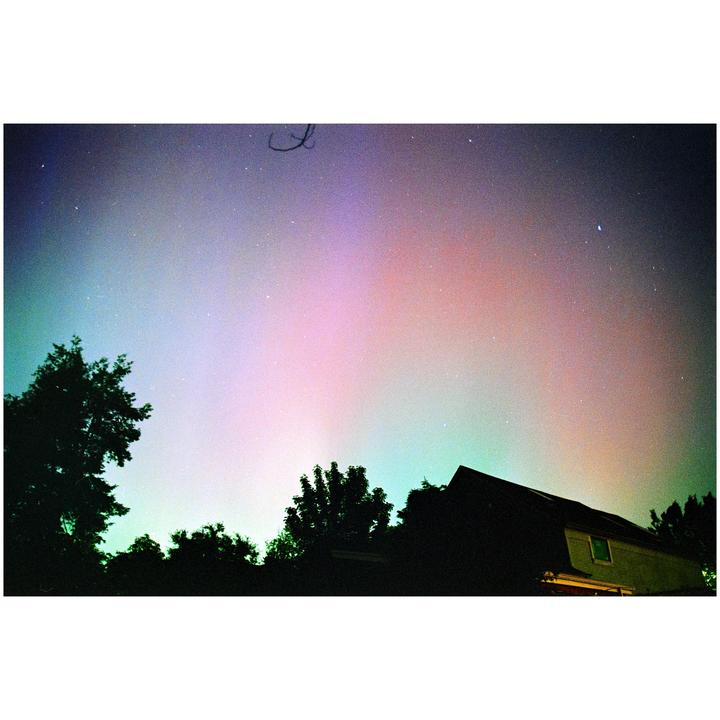 The aurora borealis glows in the night sky above a house and trees.