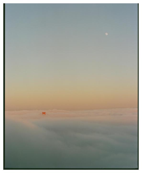 The Golden Gate Bridge is visible through a thick layer of fog with the moon in the sky above.
