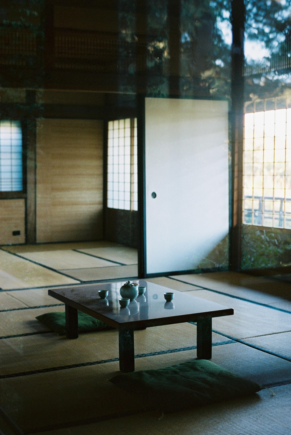 A low table with a teapot and cups sits on a tatami mat floor in a room with sliding doors and windows.