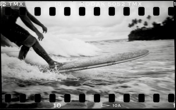 A surfer rides a wave on a surfboard with a tropical island in the background.