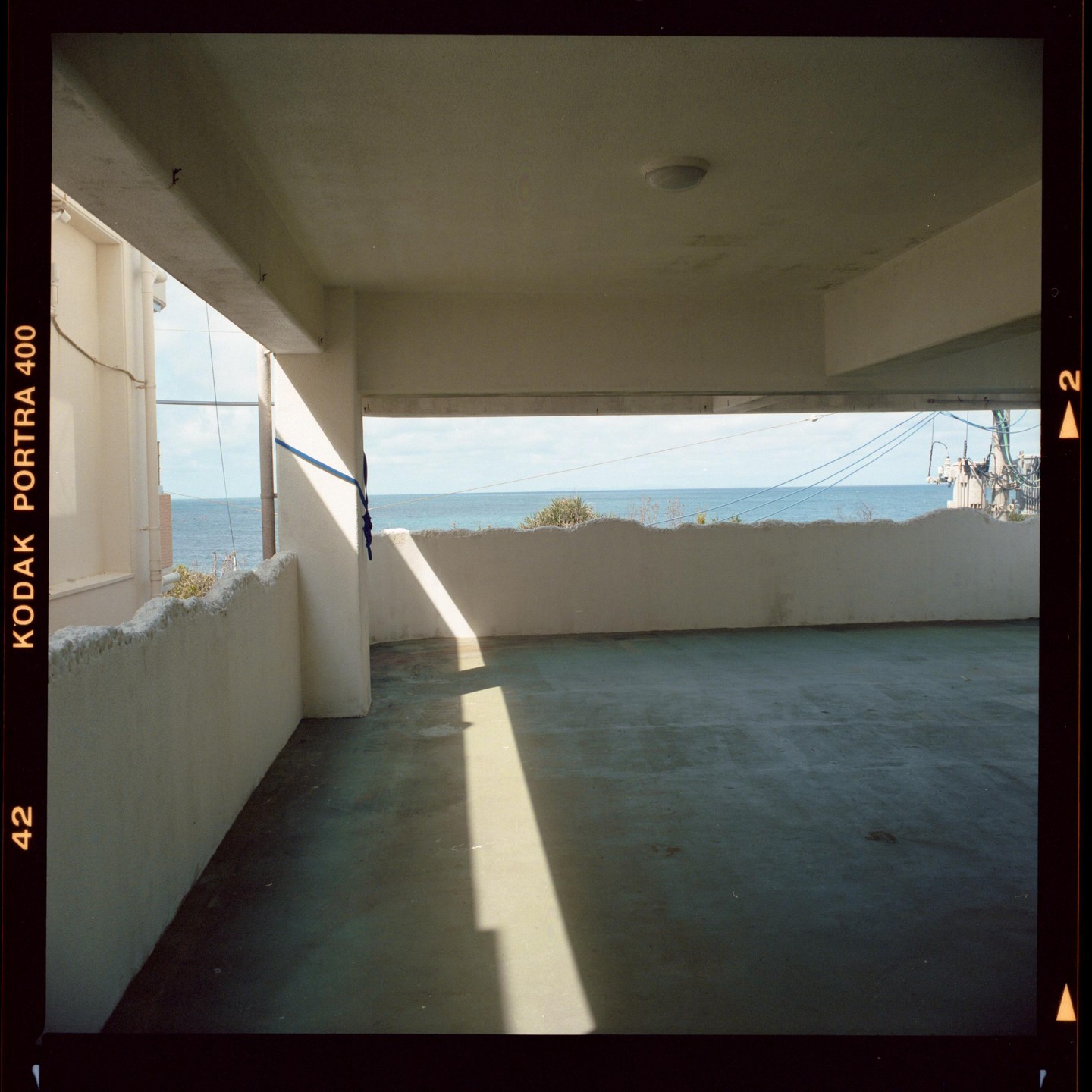 Sunlight casts a long shadow across a concrete floor with the ocean visible in the distance.