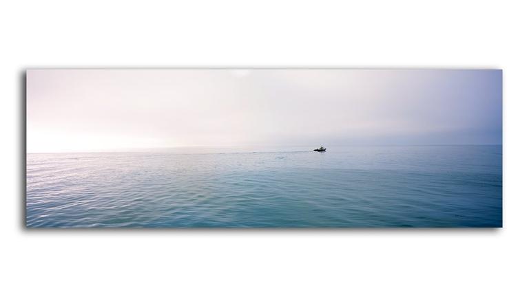 A small boat moves across a calm body of water under a hazy sky.