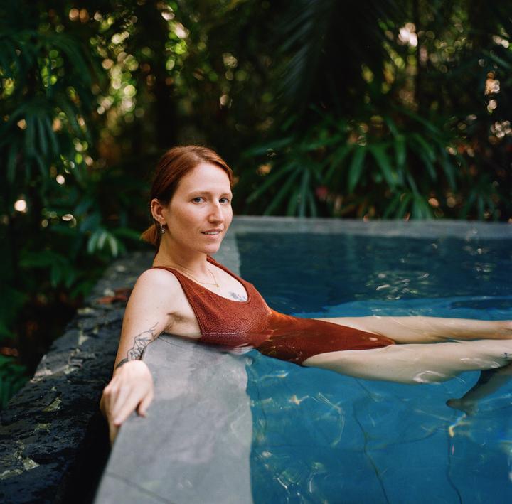 A woman in a brown swimsuit is relaxing in a pool surrounded by lush green foliage.
