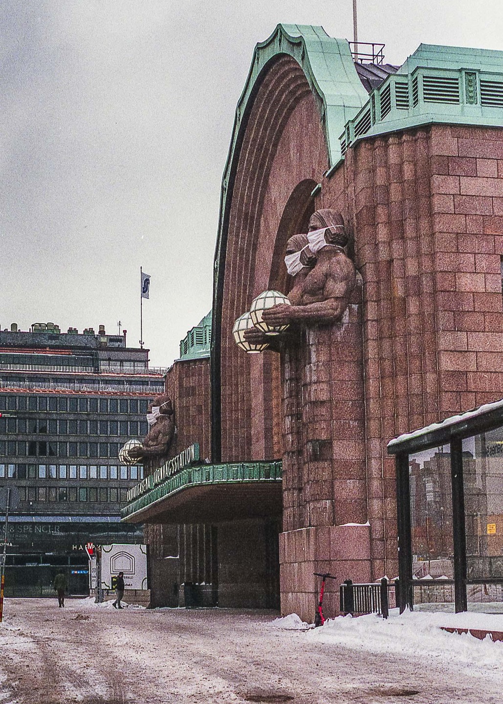 A large stone building with statues wearing face masks stands next to a snowy street.