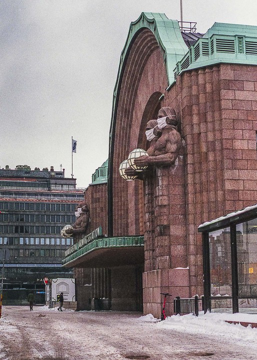 A large stone building with statues wearing face masks stands next to a snowy street.