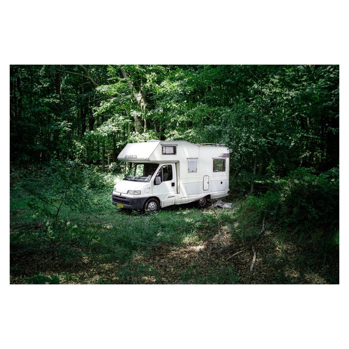 A white camper van is parked in a forest clearing surrounded by green trees and foliage.