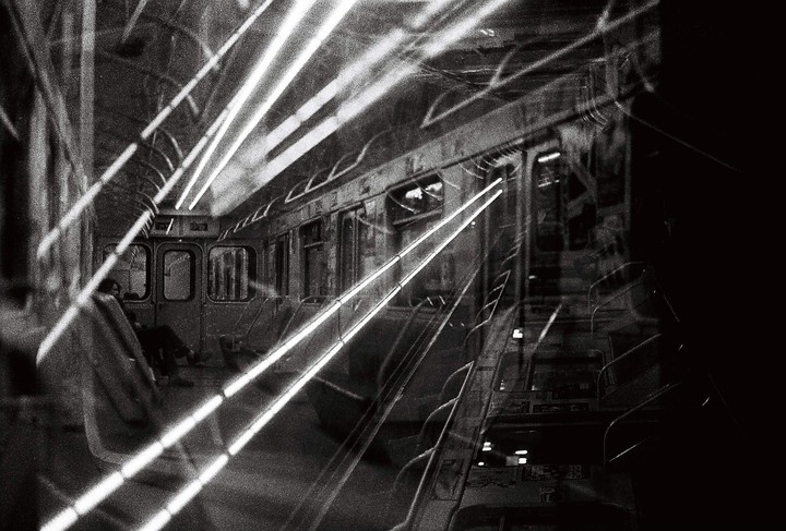 Bright light streaks cross the interior of a subway car where a person is seated.