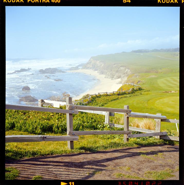 A wooden fence overlooks a sandy beach and a golf course under a hazy sky.