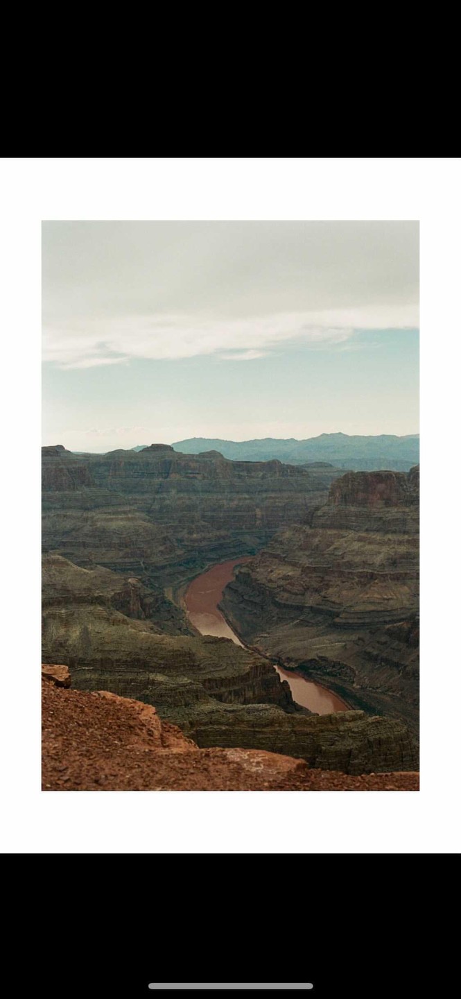 A wide river flows through a deep canyon under a cloudy sky.