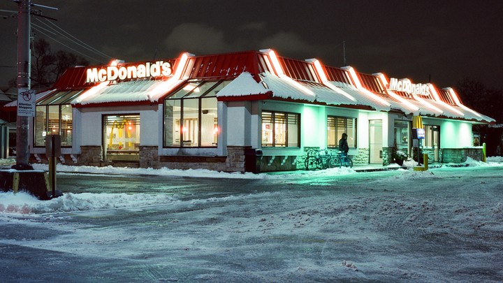 A McDonald's restaurant with snow on its roof and on the ground is illuminated at night.