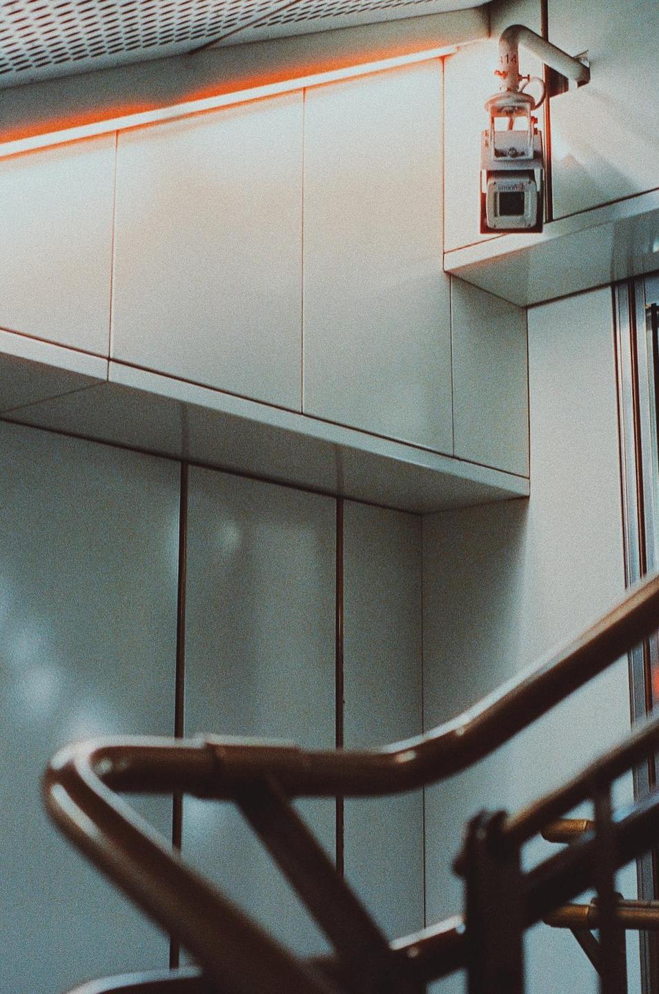 A security camera is mounted on a white wall above a railing.