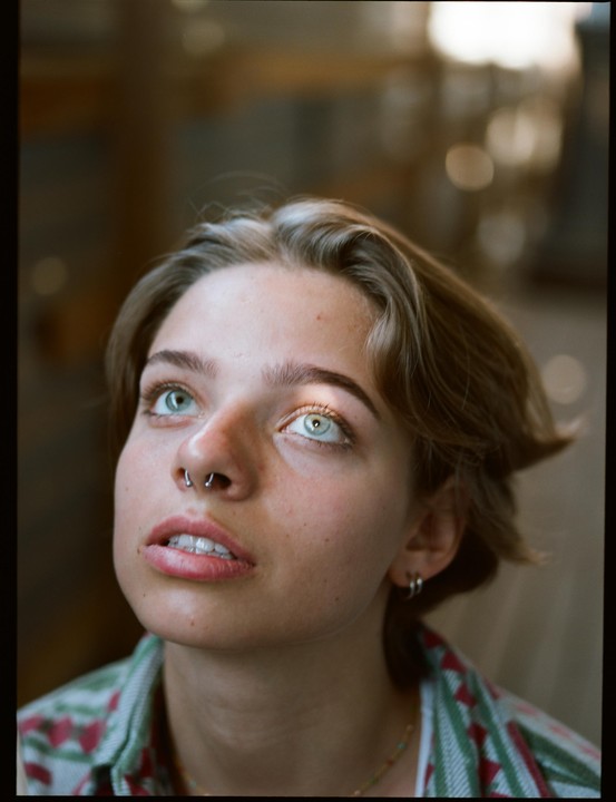 A woman with a nose ring looks up with light reflecting in her eyes.