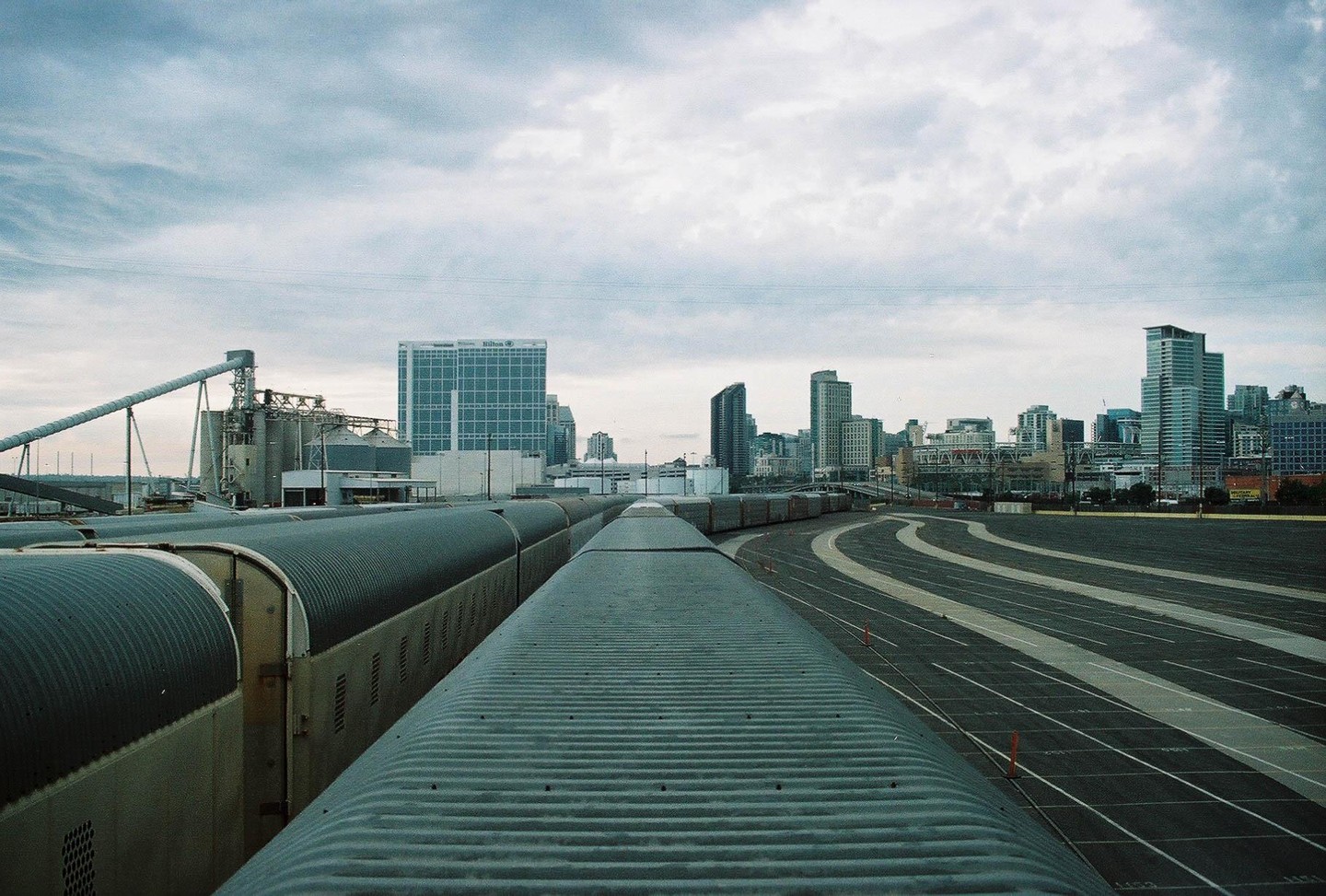 A train is parked on tracks next to a city skyline under a cloudy sky.