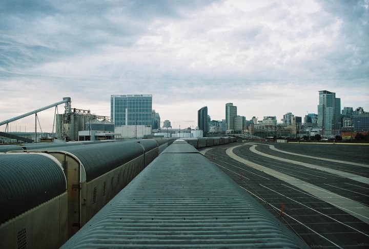 A train is parked on tracks next to a city skyline under a cloudy sky.
