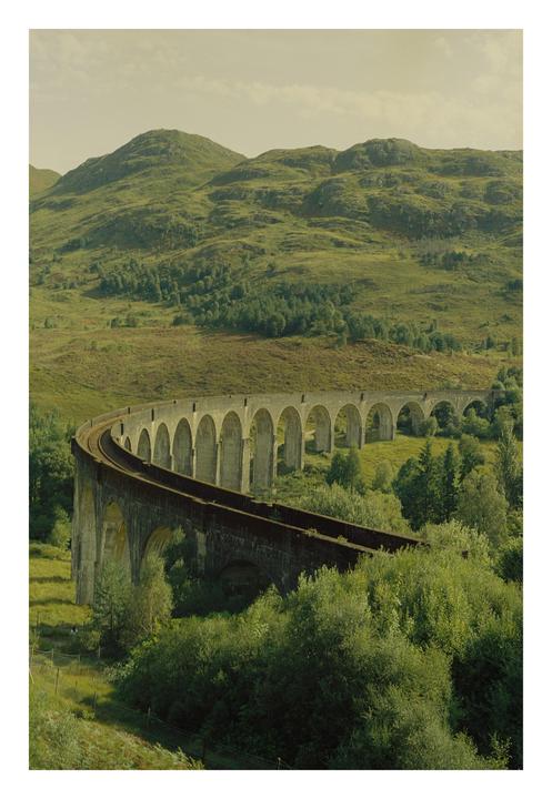 A long, curving railway viaduct with many arches spans a green valley with hills in the background.