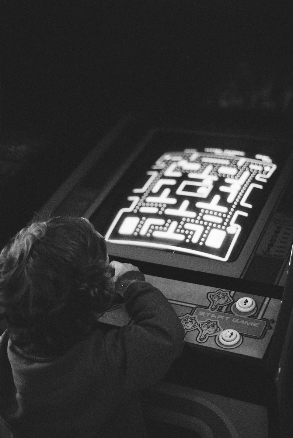A child plays a Pac-Man arcade game in a dark room.