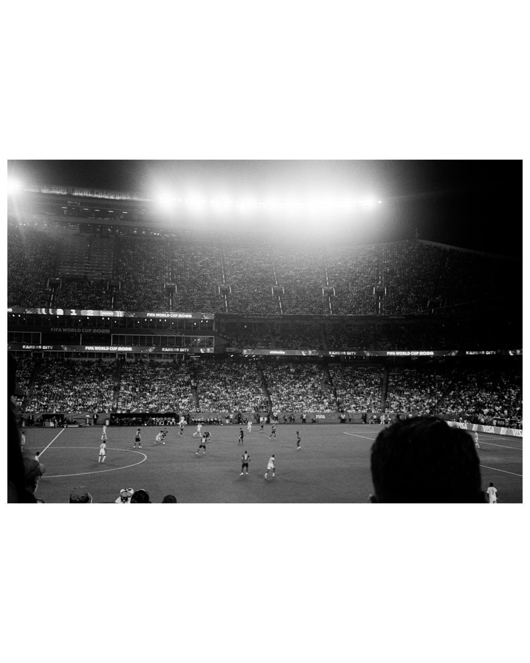 A soccer match is underway in a stadium filled with spectators under bright lights at night.