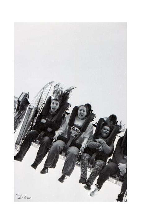 Three children with their hair flying are screaming on a fairground ride.
