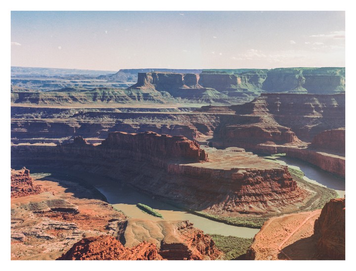 A river winds through a deep canyon with layered rock formations under a clear sky.