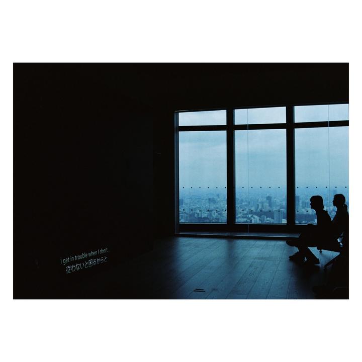 Two people sit silhouetted against a large window overlooking a city skyline, with text projected onto a dark wall.