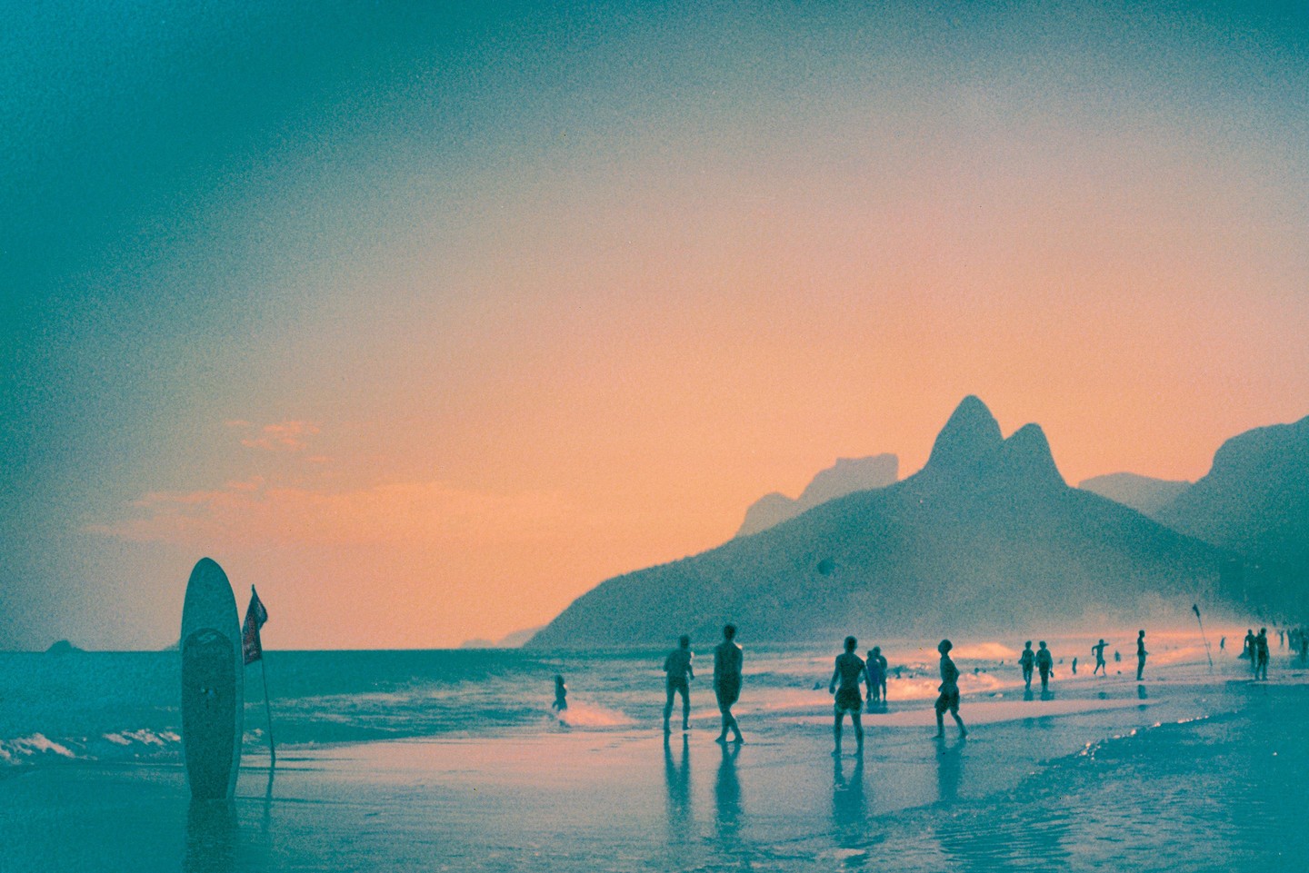 A group of people are on a beach with mountains in the background at sunset.