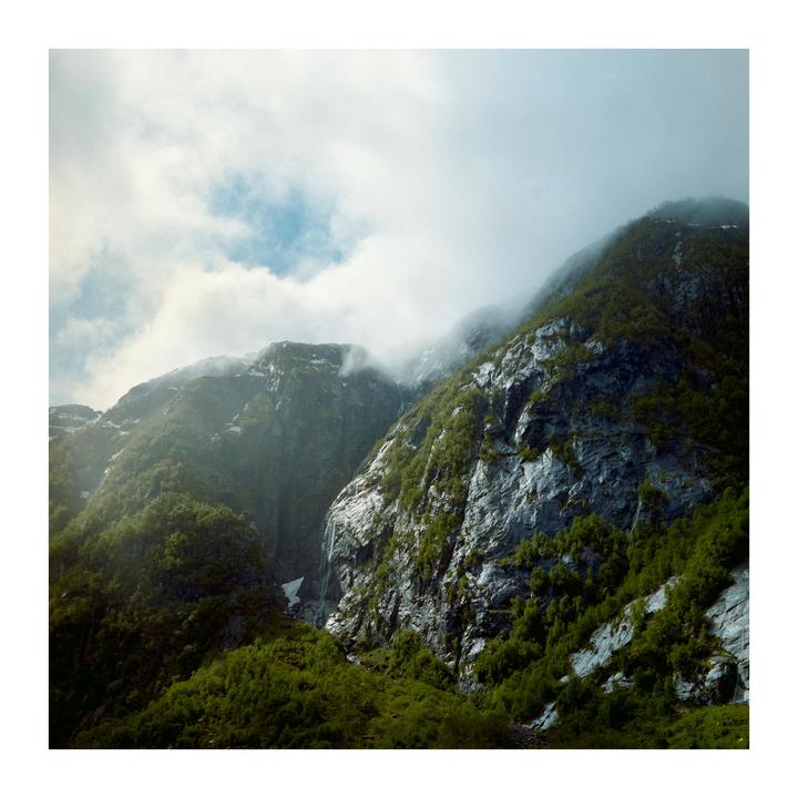 Sunlight illuminates a lush green mountain with a waterfall and mist.