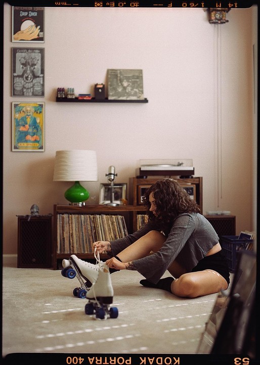 A woman sits on the floor tying the laces of a roller skate in a room with records and posters.