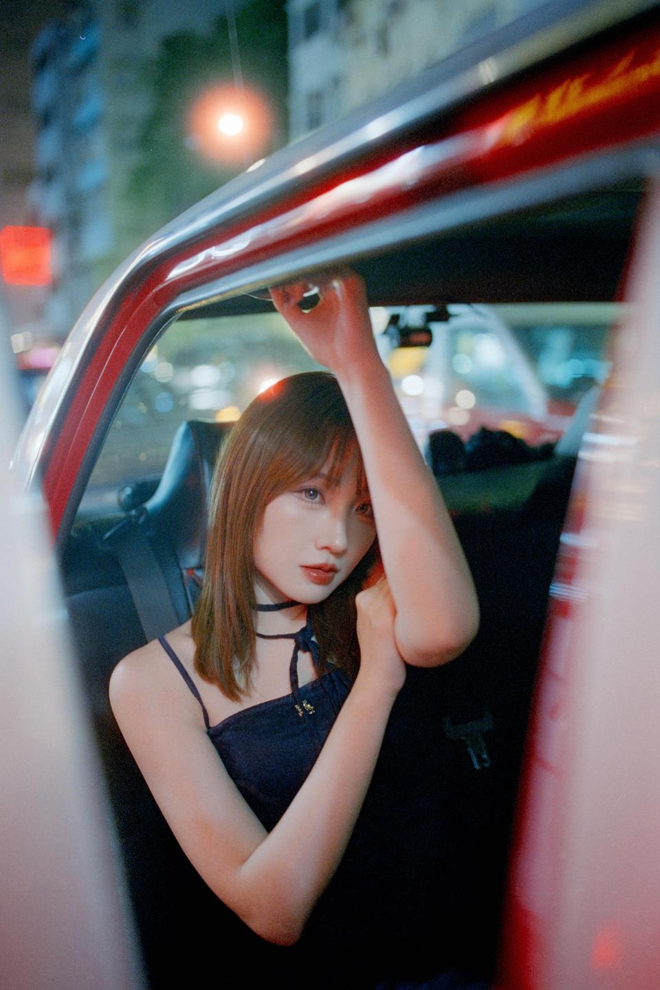 A woman sits in the back seat of a car at night with city lights visible outside.