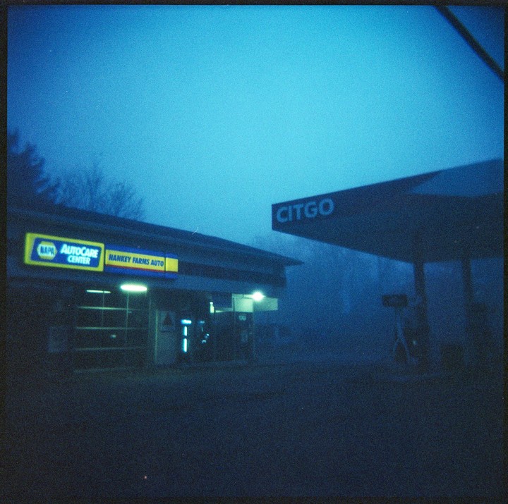 A gas station and auto repair shop are shrouded in blue fog at night.