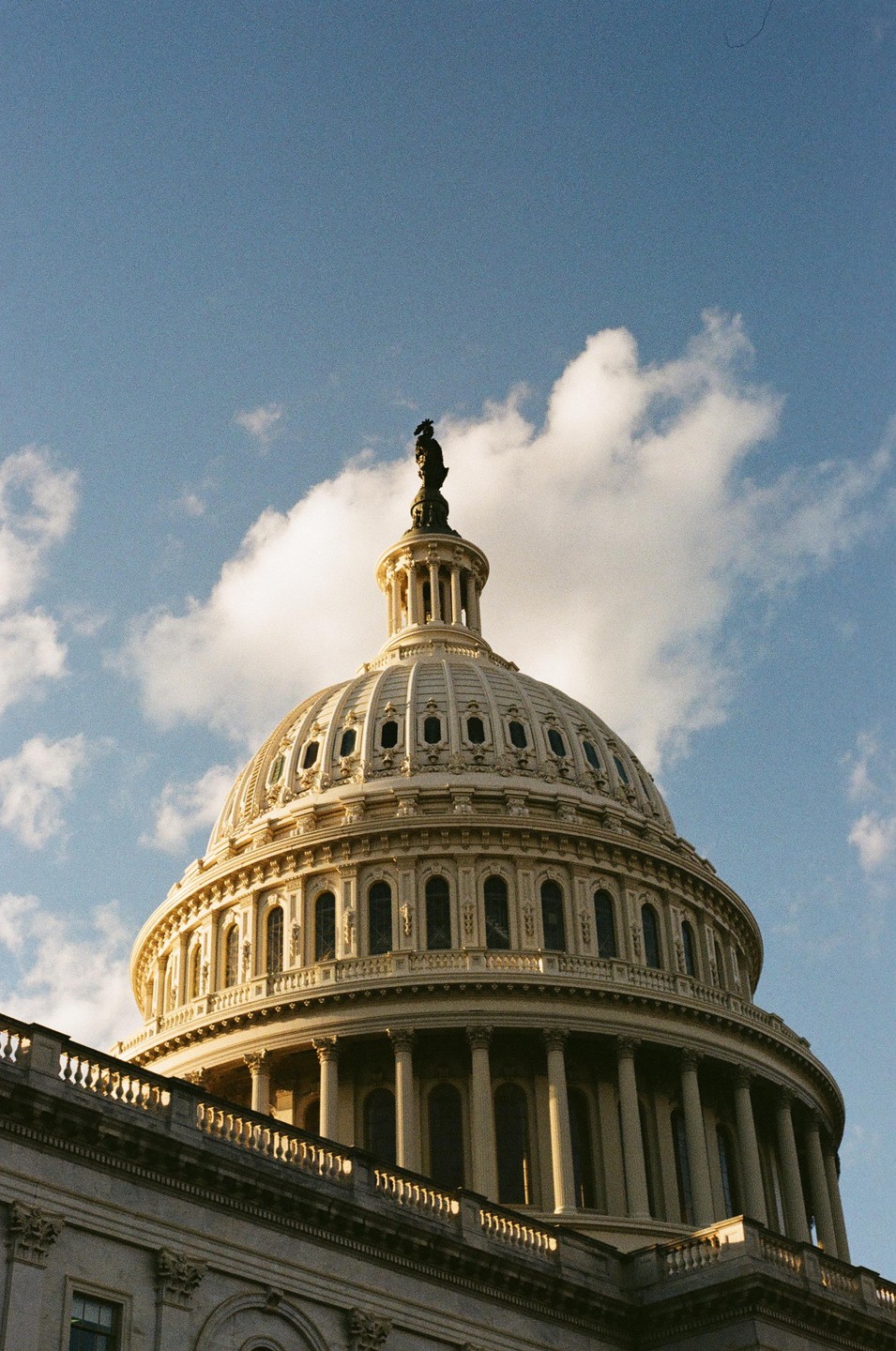 The dome of the U.S. Capitol building is visible against a blue sky with white clouds.
