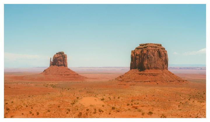Two large rock formations stand in a vast desert landscape under a clear sky.