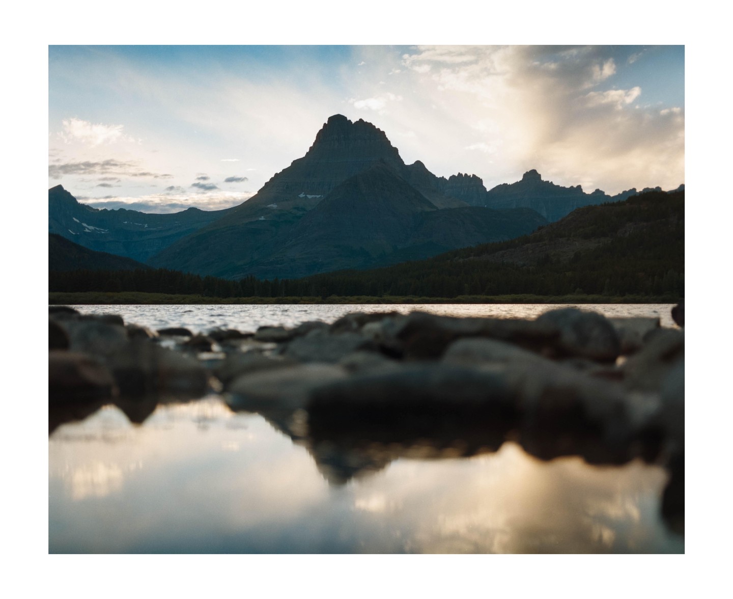 A body of water reflects the sky and mountains at dusk.