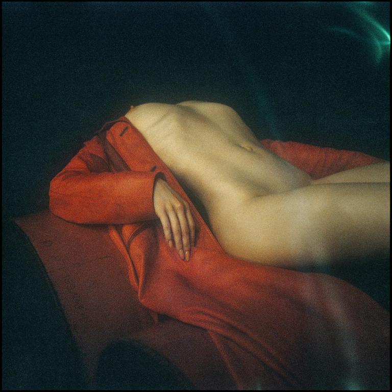 A nude woman reclines on a red garment, with her arm resting on the fabric.