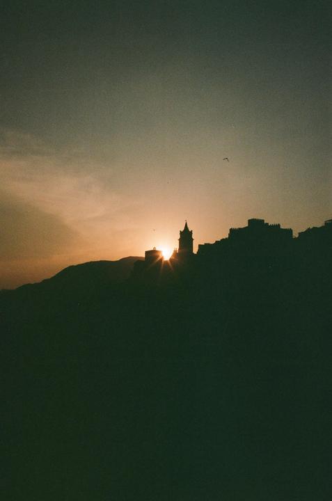 The sun sets behind a silhouetted town on a hill.