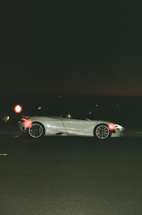 A white sports car with its lights on is parked on a dark road at night.