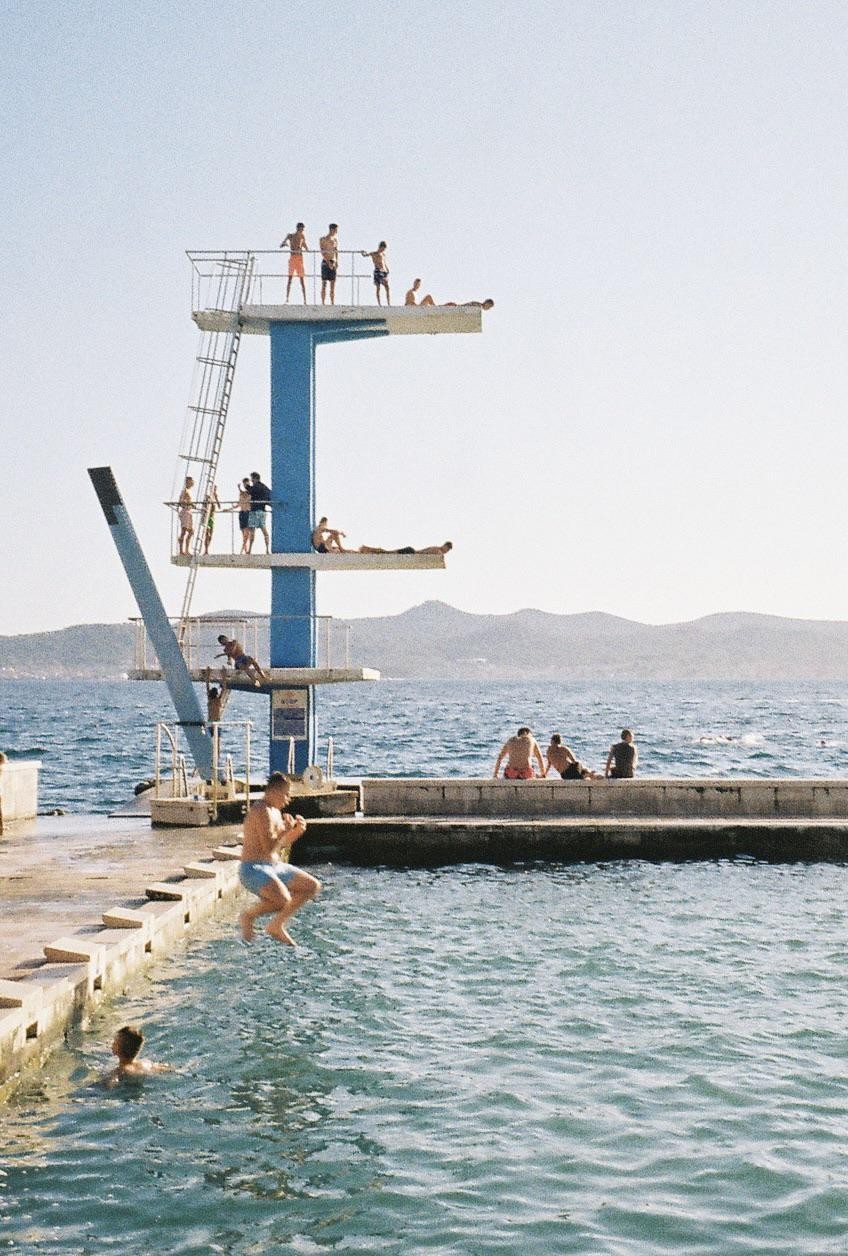 A group of men and boys are on and around a diving platform next to the ocean.