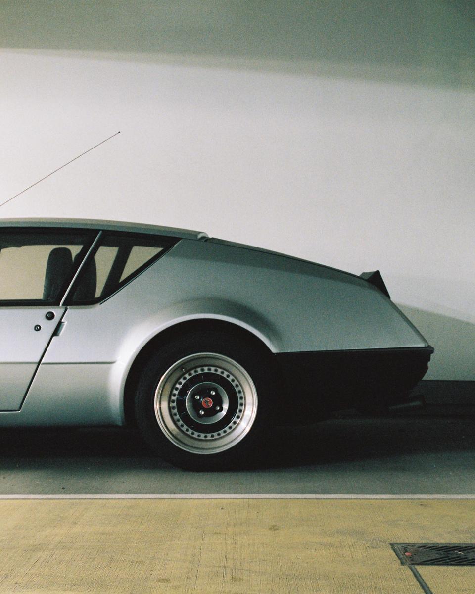 A silver car is parked in a garage, showing its side profile and rear wheel.