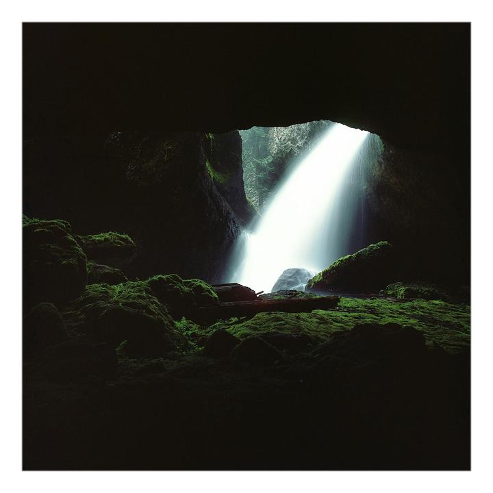 A waterfall cascades into a dark grotto covered in moss.