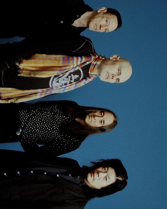 Four people are posing for a group portrait against a blue background.