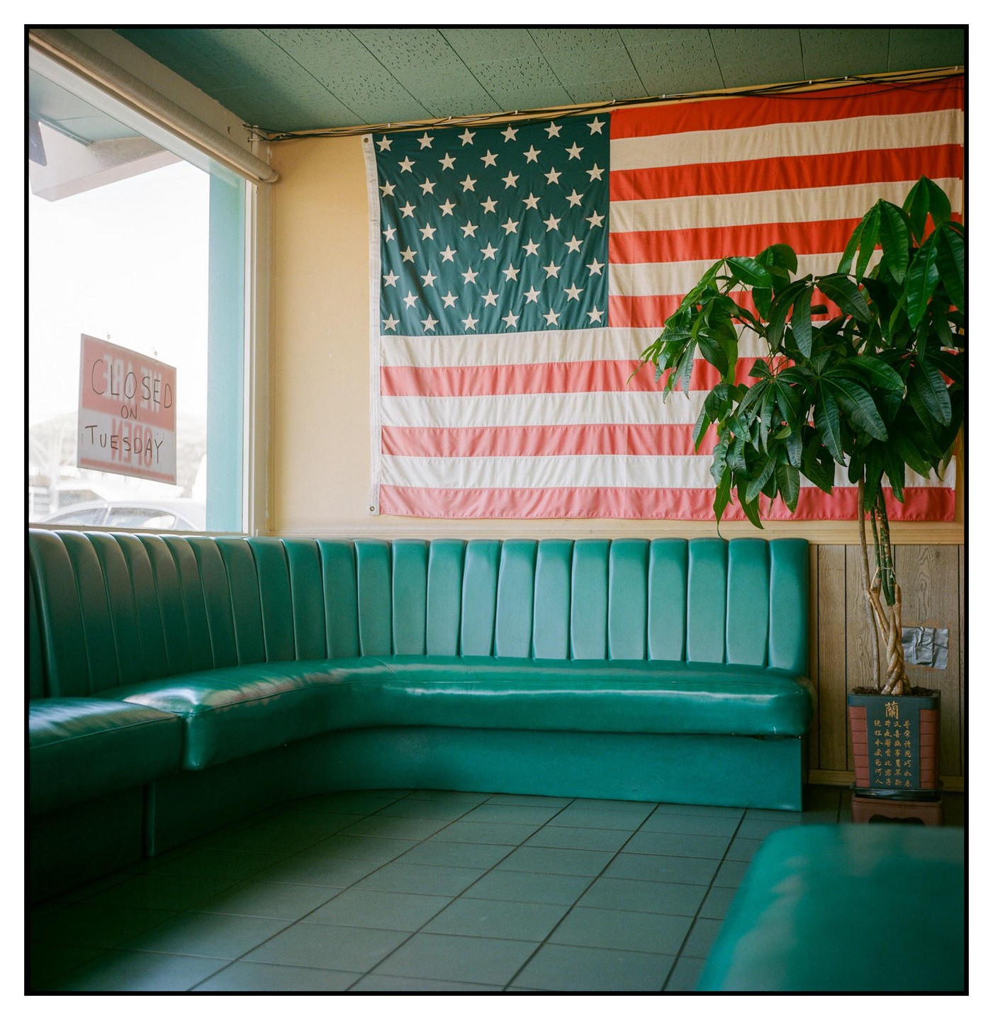 A green booth sits in a diner with an American flag hanging on the wall and a plant in the corner.