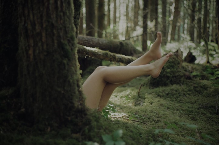 A person's legs and feet are visible among mossy trees and forest floor.