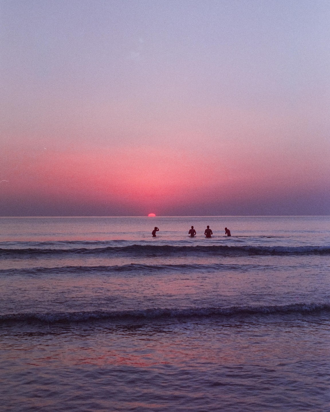 Four people are in the ocean as the sun sets over the water.