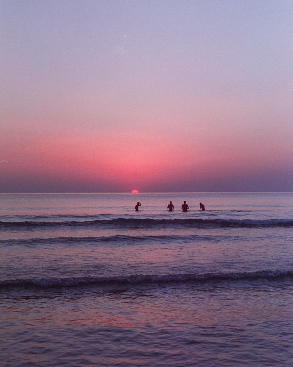 Four people are in the ocean as the sun sets over the water.