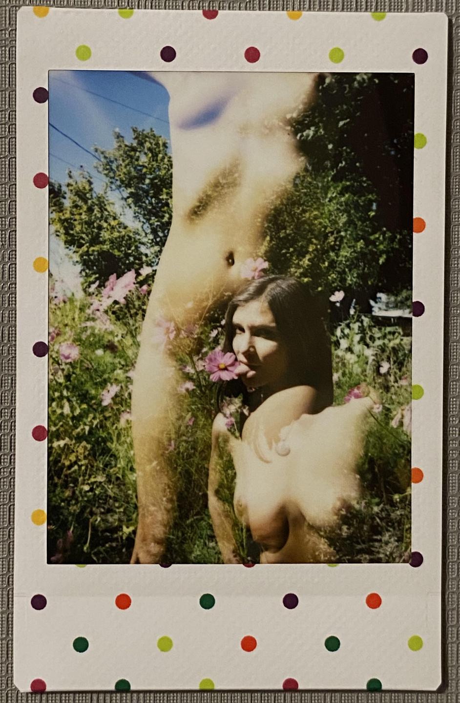 A double exposure shows a woman with a flower in her mouth and a partial nude body in a garden.