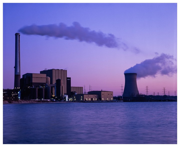 A power plant with two smokestacks emits smoke into the purple dusk sky over Lake Michigan.